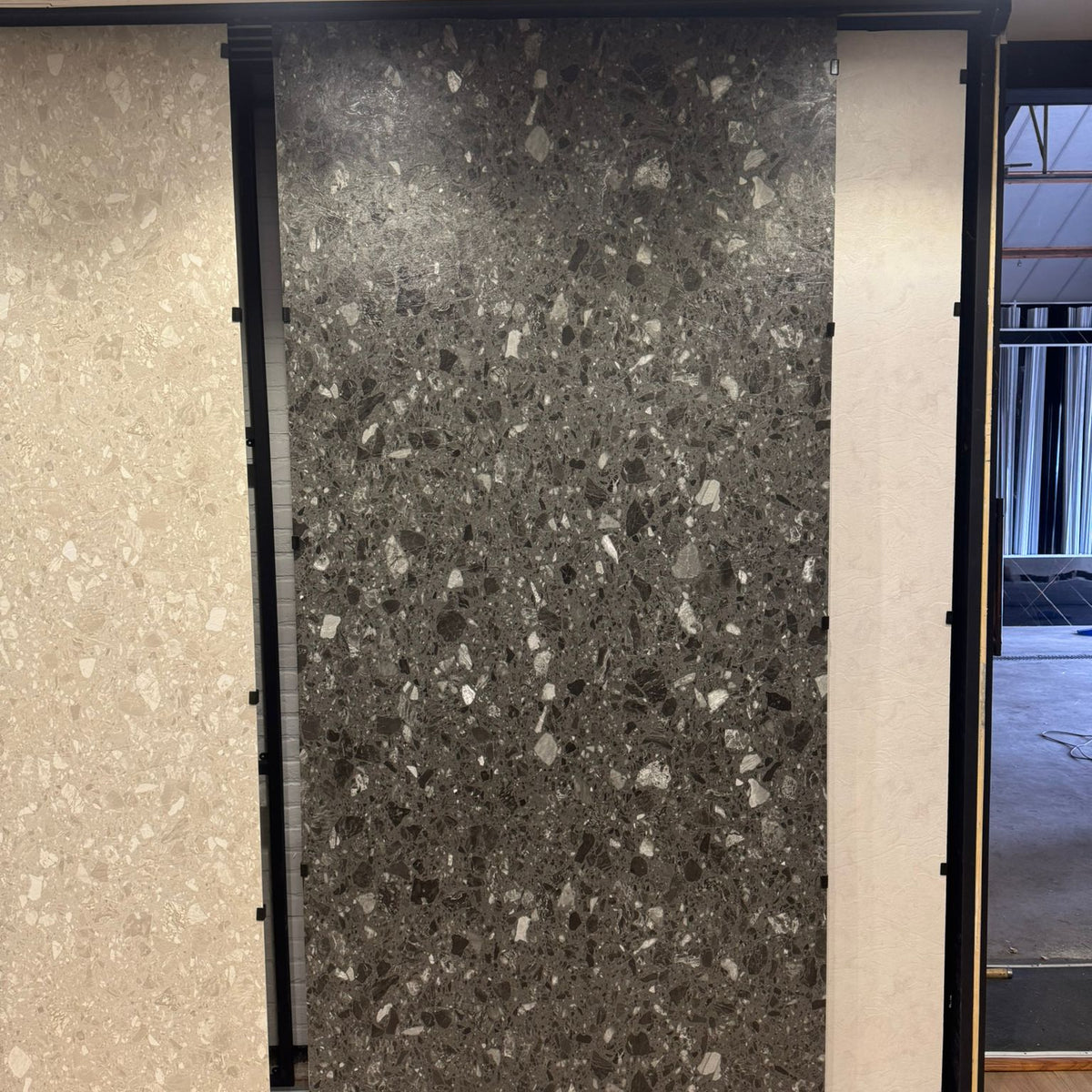 Donkergrijs terrazzo SPC wandpaneel in showroom opstelling met grote plaat en grove steenkorrels