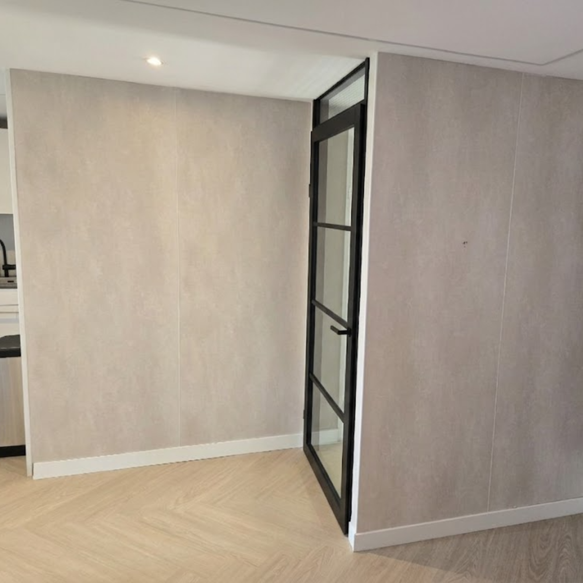 Beige betonlook SPC wandpanelen toegepast in modern interieur met strakke wandafwerking en zwarte deur